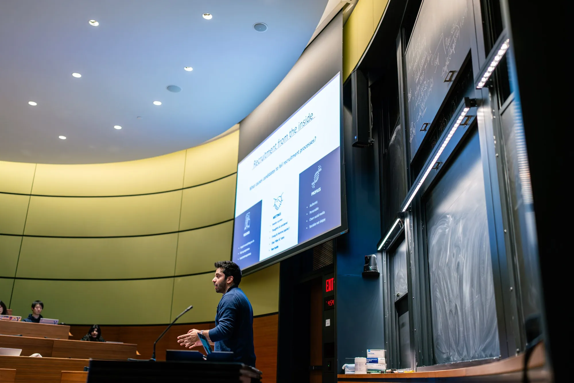 Hassan Akram presenting at a lectern in a Yale School of Management lecture theatre, beside a slide reading Recruitment from the inside.